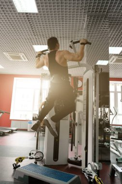 Siyah bir tişört ve pantolon bir halter kemer ile kaslı adam çekti simülatör güneşin arka görünüm