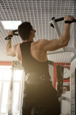 Siyah bir tişört ve pantolon bir halter kemer ile kaslı adam çekti simülatör güneşin geri görünüm aşağıdan