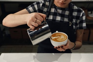 Barista kız krem cappuccino kahve ve küçük sürahi içinde elleri üzerinde sanat çizer