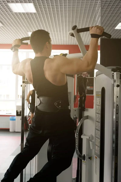 Hombre musculoso en una camiseta negra y pantalones con un cinturón de levantamiento de pesas se aprieta en la cinta de correr, vista trasera — Foto de Stock