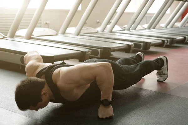 El hombre musculoso en la camiseta negra y los pantalones, de pie apretaba los puños sobre el fondo de las zapatillas — Foto de Stock