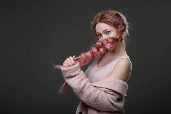 Portré zsinórra rózsaszín hajú lány, rózsaszín és kék smink, egy félkör alakú játékosan nézett a kamerába, és amely az arc zsinór sötét háttér előtt állva — Stock Fotó
