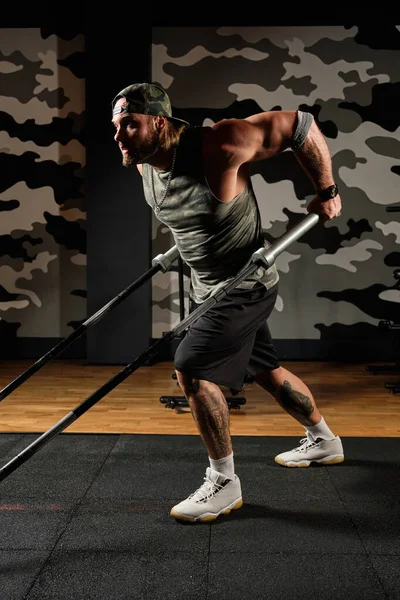 Hombre musculoso con uniforme deportivo hace un ejercicio sobre sus hombros sosteniendo las barras de una barra — Foto de Stock