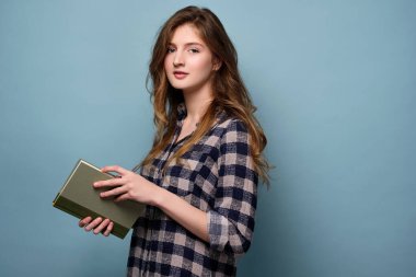 Ekoseli tişörtlü bir kız elinde bir kitapla dikiliyor ve çerçevenin içine bakıyor..