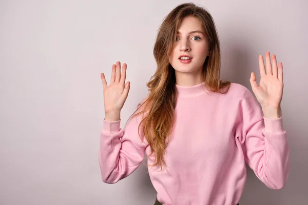 La chica en camiseta rosa de pie sobre un fondo claro, boca sorprendida abierta mirando a la cámara, levantando las manos . — Foto de Stock