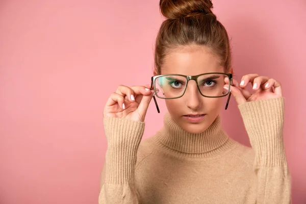 핑크 색 배경에 스웨터를 입고 안경 렌즈를 바라보고 있는 한 소녀가 안경을 그 의 앞에 들고 눈에 집중하고 있습니다 — 스톡 사진