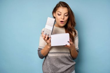 Esmer kadın sürpriz bir şekilde ağzını açtı ve mavi bir arka planda duran hediye kutusuna baktı..