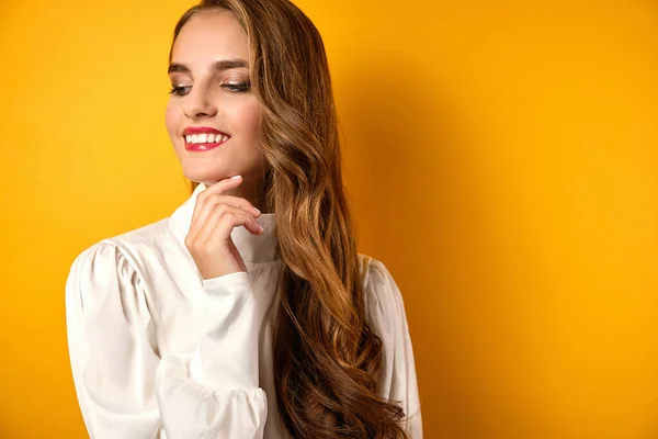 Una chica con los labios rojos y rizos en una blusa blanca se para sonriendo y mira hacia otro lado sobre un fondo amarillo . — Foto de Stock