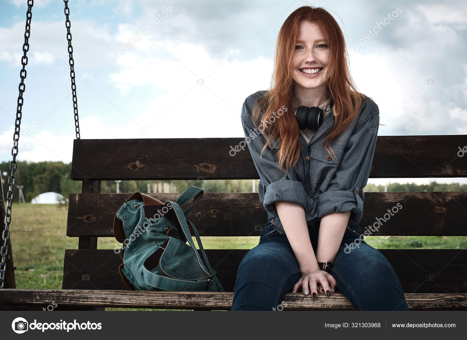 Redhead Girl In A Denim Shirt Sits With A Backpack On A Wooden