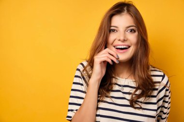 Çizgili tişörtlü tatlı esmer sarı arka planda gülüyor..