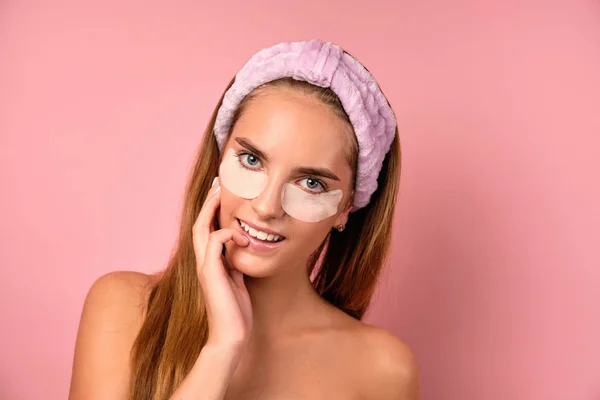 Potret seorang gadis dengan handuk ungu dan dengan tambalan di bawah matanya melihat dalam bingkai pada latar belakang merah muda — Stok Foto