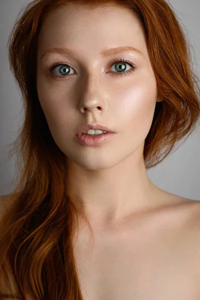 Een close portret van een roodharig meisje met sproeten en blauwe ogen, met stralende huid en los haar op haar blote schouders. — Stockfoto