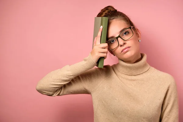 En flicka med ren hud och en hög stråle i glasögon med ett trött ansikte och tittar på bilden med sin bok på huvudet — Stockfoto