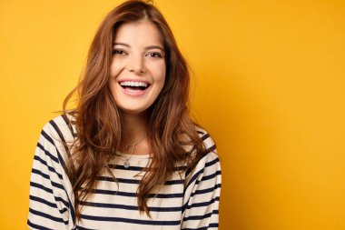 Çizgili tişörtlü çekici bir esmer sarı arka planda duruyor ve neşeyle gülüyor.