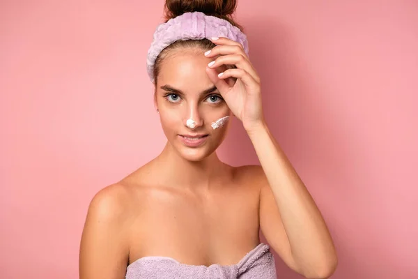 Seorang gadis cantik menyesuaikan perban di kepalanya berdiri di latar belakang merah muda dan tersenyum dengan noda krim di wajahnya — Stok Foto