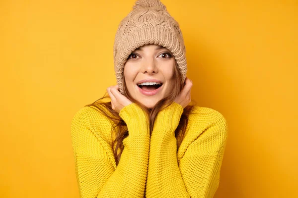 En brunett i gul tröja står på en gul bakgrund och skrattar, drar ner hatten. — Stockfoto