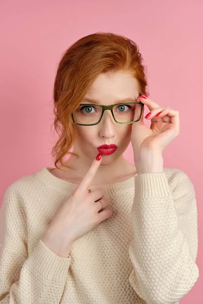 Röd-hårig flicka med rött läppstift och manikyr justerar sina glasögon och ser i ramen, sätta fingret på hennes läppar — Stockfoto