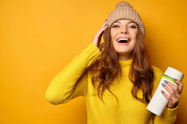 Güzel esmer, sarı bir süveter içinde temiz bir ten görüyor ve sarı bir arka planda duran şapka neşeyle gülerek termokupa tutuyor.