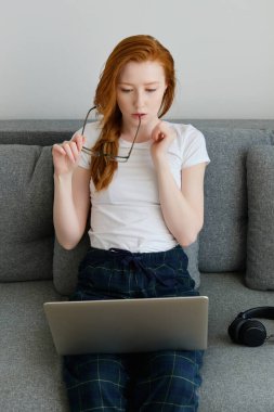 Pijamalarıyla kanepede oturan kız, gözlüklerinin bir deliğini laptopa incelikle yapıştırıyor. Çerçeve üstte