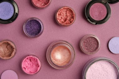 Parıltılar, rujlar, dudak parlatıcıları, göz gölgeleri ve pudra kirli pembe desenli bir arka plana yerleştirilir.