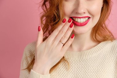 Kadın elinin yakın çerçevesi kırmızı leke ve rujla, pembe arka plandaki kırmızı kızın gülüşü. 