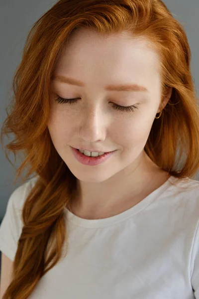 Portret van een roodharig meisje in een wit T-shirt glimlachend met gesloten ogen — Stockfoto
