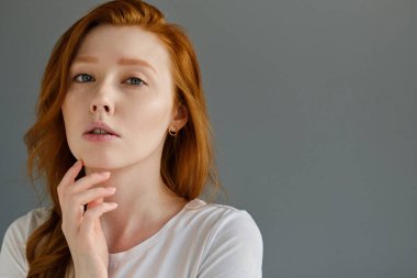 Kafasından vur. Kızıl saçlı bir kız gri bir arka planda duruyor, parmaklarını kaldırarak çenesini kaldırıyor ve çerçeveye bakıyor.