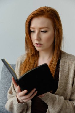 Güzel, kızıl saçlı bir kız onu önünde tutan siyah kitabı dikkatle okuyor..