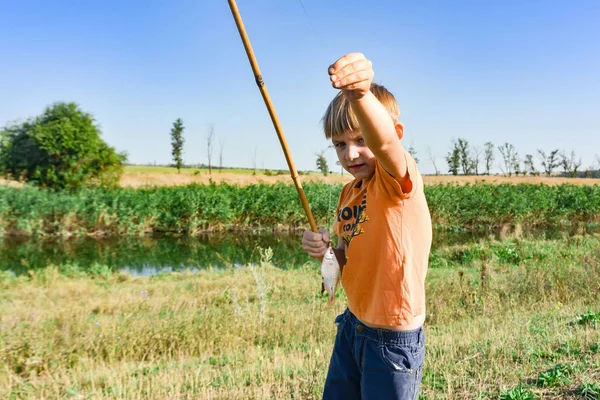 Un ragazzo di pesca è alla ricerca di una canna da pesca, un ragazzo felice e gioioso su un fiume . — Foto Stock