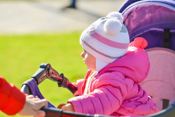 Kırmızı ceketli, beyaz şapkalı küçük neşeli bir kız sonbahar parkında bebek arabasına biniyor.. — Stok fotoğraf