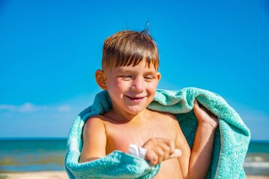 Kumsaldaki çocuk bir havluyla saklanır ve denizde yüzdükten sonra kendini deniz suyundan siler..
