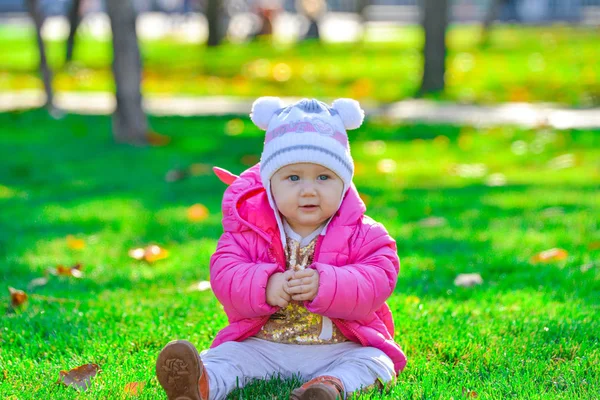 Little joyful girl in a red jacket sits on the green grass. — Stock Photo, Image