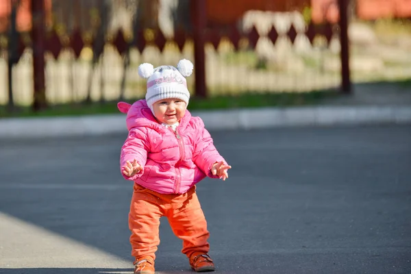 Une petite fille en veste rouge apprend à marcher sur la route l'après-midi d'automne . — Photo