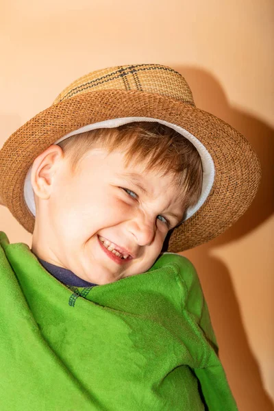 Menino alegre e feliz em um chapéu de palha e roupas verdes sorrindo e olhando para a câmera . — Fotografia de Stock