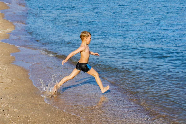 Un garçon court dans l'eau sur le bord de la mer . — Photo