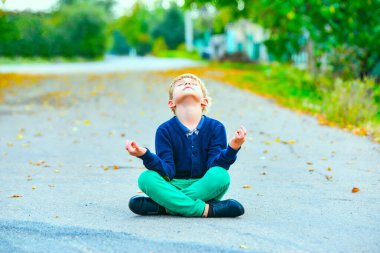 Çocuk sokakta lotus pozisyonunda oturur ve kafasını havaya kaldırarak meditasyon yapar..