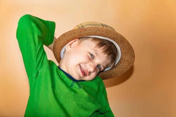 지푸라기 모자를 쓰고 녹색 옷을 입고 웃으며 카메라를 보며 즐겁고 행복해 하는 소년. — 스톡 사진