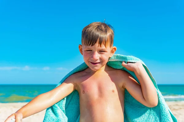 De jongen op het strand verbergt zich met een handdoek en veegt zichzelf van het zeewater na het zwemmen in de zee. — Stockfoto