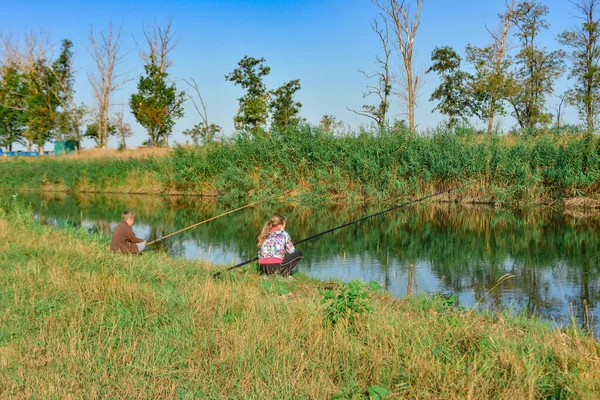 Мальчик и девочка сидят на берегу реки и ловят удочки. . — стоковое фото