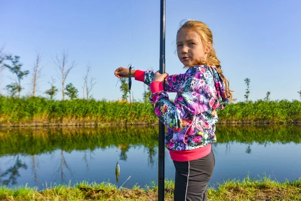 Ein Mädchen mit Angelrute zeigt einen gefangenen Fisch. — Stockfoto