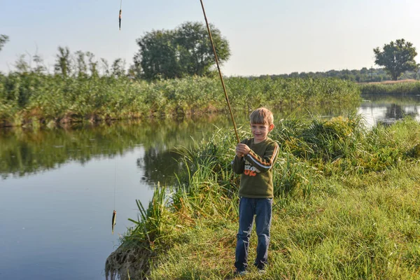 Egy vidám és boldog fiú örül első halfogásának egy horgászboton a folyón.. — Stock Fotó