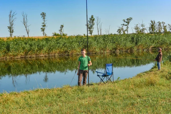 Молодой человек стоит с удочкой на берегу реки для рыбалки . — стоковое фото