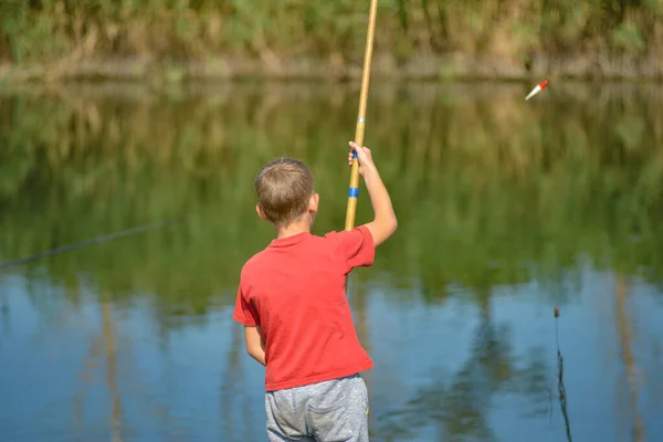 Un ragazzo in camicia rossa getta una canna da pesca sul fiume cattura . — Foto Stock