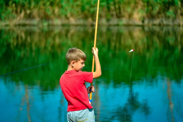 Un ragazzo in camicia rossa getta una canna da pesca sul fiume cattura . — Foto Stock