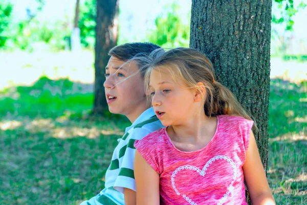 Ένα αγόρι και ένα κορίτσι κάθονται κάτω από ένα δέντρο και μιλάνε μεταξύ τους, μιλάνε μεταξύ τους.. — Φωτογραφία Αρχείου