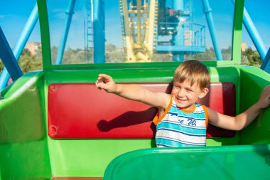 Dönme dolaba binen neşeli çocuk yan tarafta elini gösteriyor..