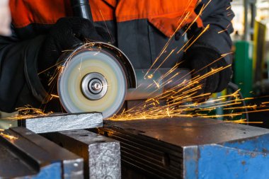 İşçi, metali elektrik açı öğütücüsüyle keser, kıvılcımlar uçuşur..