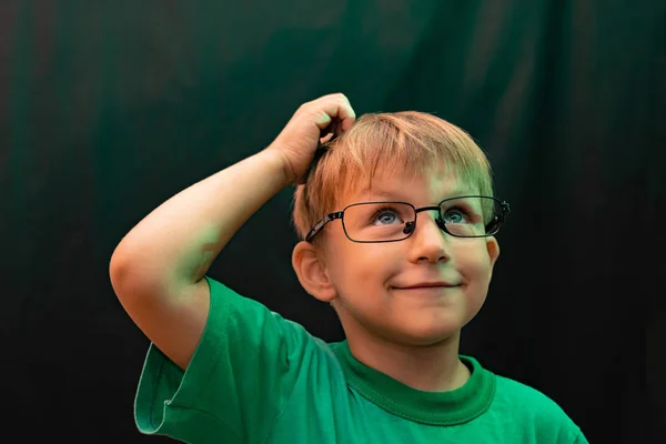 Překvapený chlapec v brýlích na černém pozadí drží ruku ve vlasech a dívá se nahoru — Stock fotografie