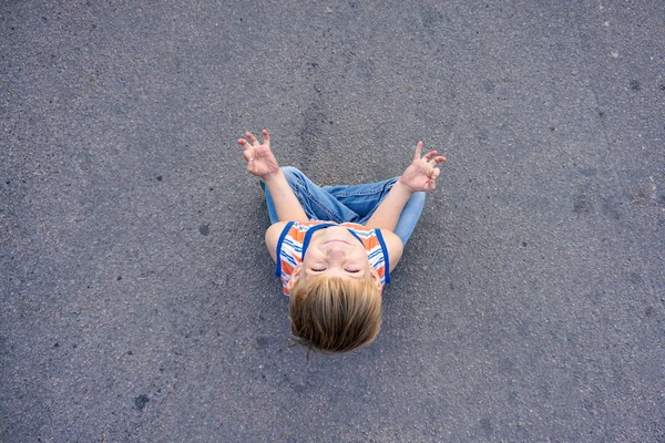 Un niño está meditando sentado en el asfalto en medio de la carretera . — Foto de Stock