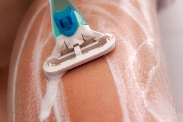 Mädchen rasiert sich mit Rasiermesser die Beine und verteilt Schaum darauf — Stockfoto